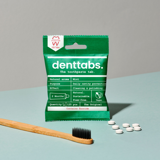 Packaging of denttabs with a wooden toothbrush and white tablets on a light blue surface.