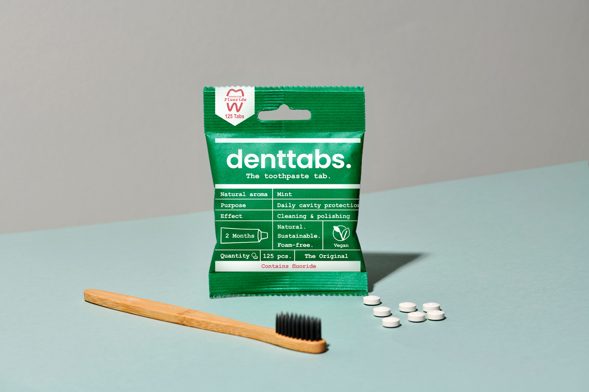 Packaging of denttabs with a wooden toothbrush and white tablets on a light blue surface.